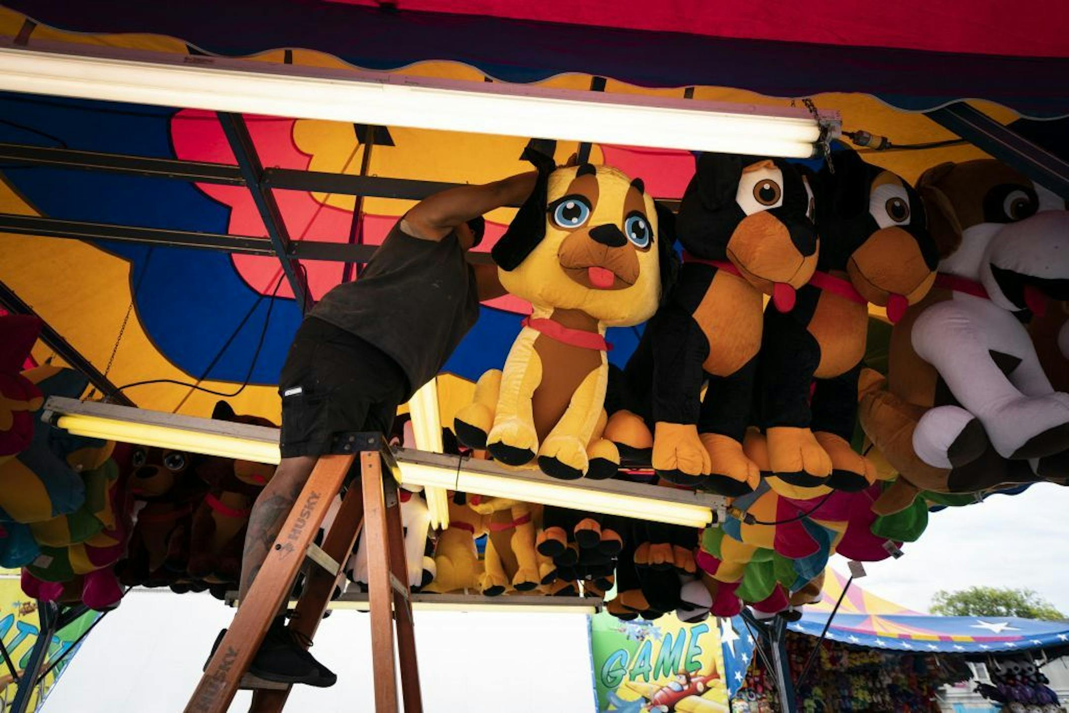 Lorraine Robitaille, right, handed Margarita Nunez a large stuffed dog as they hung game prizes at their stand in the Midway on Wednesday, ahead of the opening of the Minnesota State Fair.