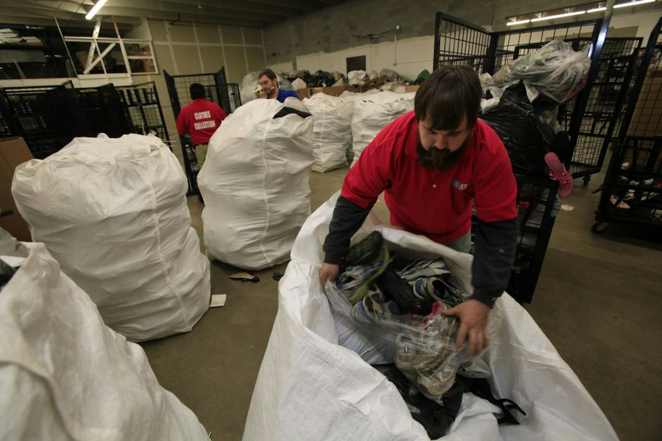 (Left to right) Cornellio Gaviian (back to camera), Warehouse Manager Anthony Gasper (blue shirt) and Ross Holland of USAGAIN put donated shoes into white bags to be shipped at the New Brighton, MN plant on October 30, 2012.