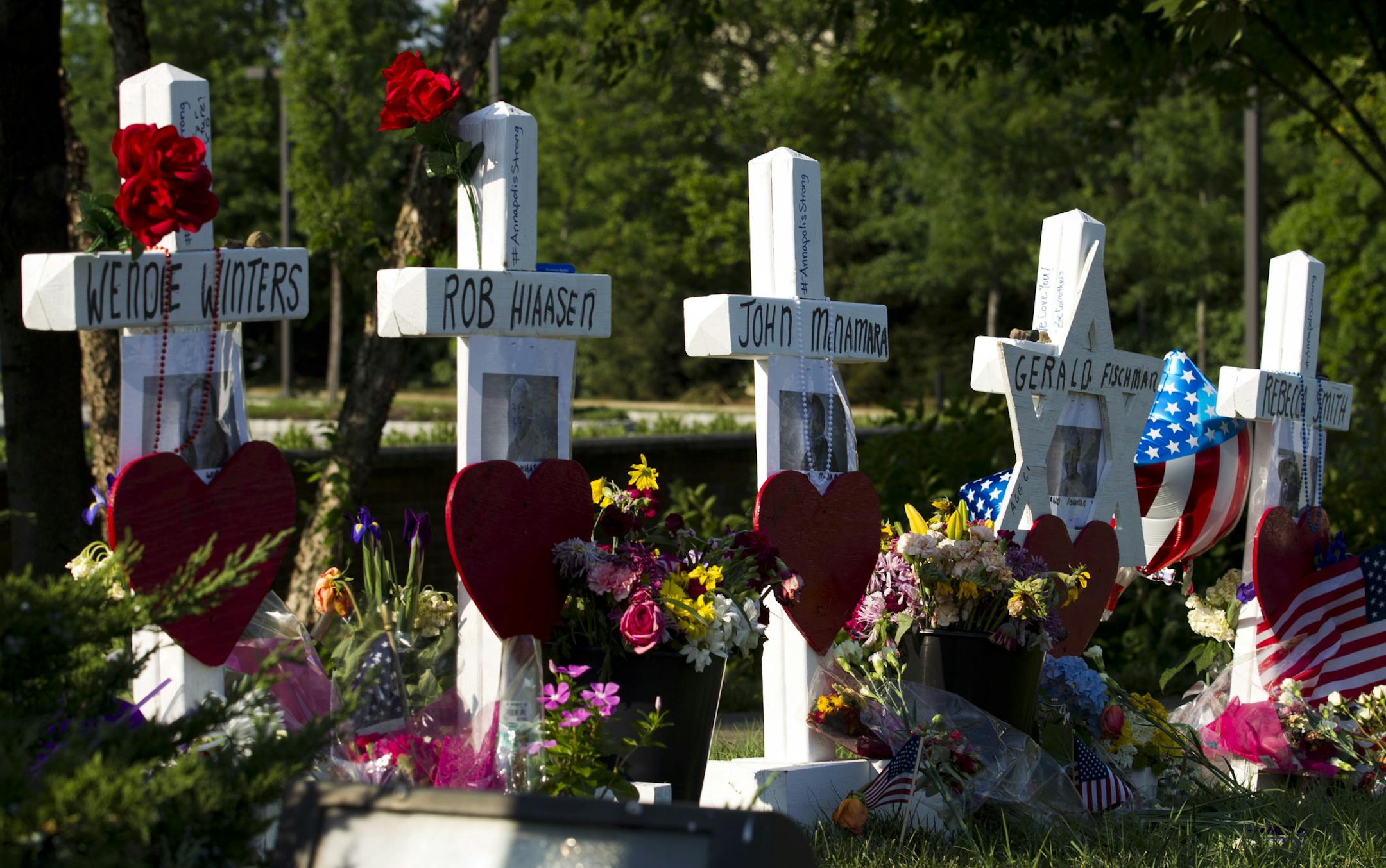 An American flag is placed next to five crosses representing the people killed in a newsroom shooting, at a makeshift memorial at the scene outside the office building housing The Capital Gazette newspaper in Annapolis, Md., on Sunday, July 1, 2018. Jarrod Ramos is charged with murder after police say he opened fire Thursday at the newspaper. (AP Photo/Jose Luis Magana)