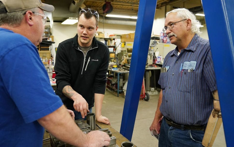 Justin Vandevoort, center, talked with machinist Rod Sammon, left, and press department lead Ben Froman, right, as they worked with a metal stamping d