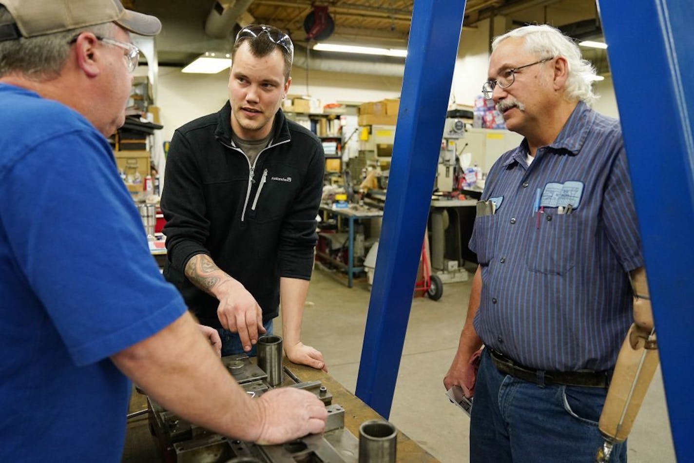 Justin Vandevoort, center, talked with machinist Rod Sammon, left, and press department lead Ben Froman, right, as they worked with a metal stamping die.