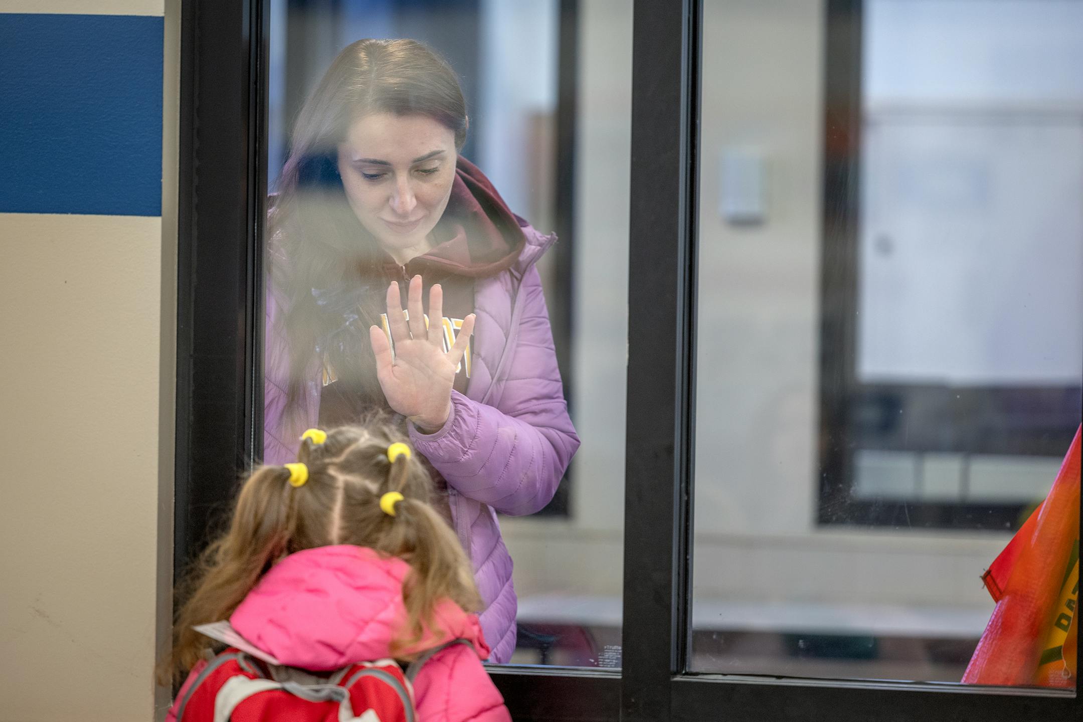 Ukrainian refugee Natalia Kuchma waves goodbye to her five-year-old daughter Solomiia Kuchma at the Lake Harriet Community School's Lower Campus in Minneapolis, Minn., on Monday, Oct. 24, 2022.  Natalia has to stand at a window several minutes at drop-off so Solomiia can get used to being left at the school.  She struggles with separating from her mother.