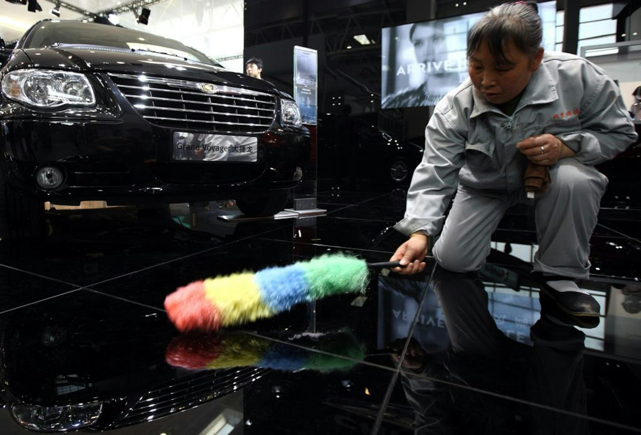 A worker cleans the floor in front of Chrysler Group LLC's Grand Voyager vehicle at the Beijing Auto Show in Beijing, China, on Saturday, April 24, 2010. The show will be held through April 27. Photographer: Tomohiro Ohsumi/Bloomberg