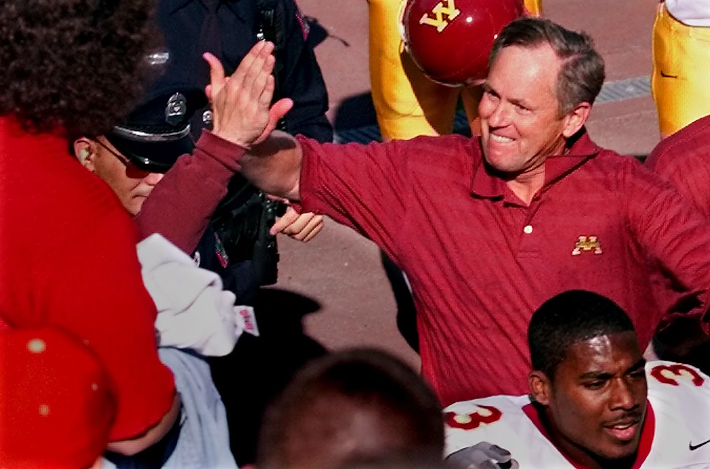 Gopher head coach reacts to a congratulatory high-five thrown by fans as he leaves the field with a victory over Ohio State. In the foreground is Gopherf player Ron Johnson.