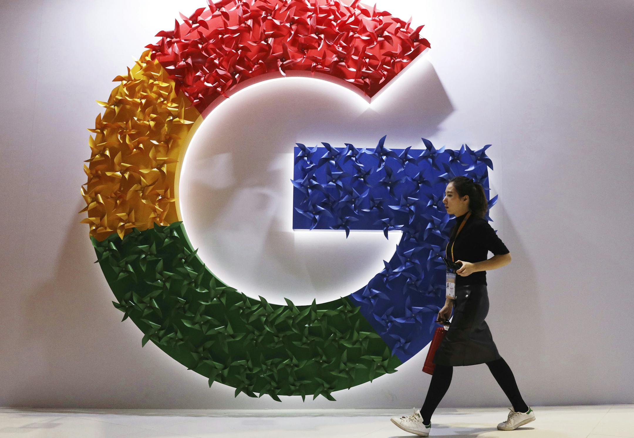 FILE - In this Monday, Nov. 5, 2018 file photo, a woman walks past the logo for Google at the China International Import Expo in Shanghai. By U.S. standards, the Justice Department's move to sue Google this week for abusing its dominance in online search and advertising was a bold move. But it treads on ground already broken years before by EU officials in Brussels. (AP Photo/Ng Han Guan, File)