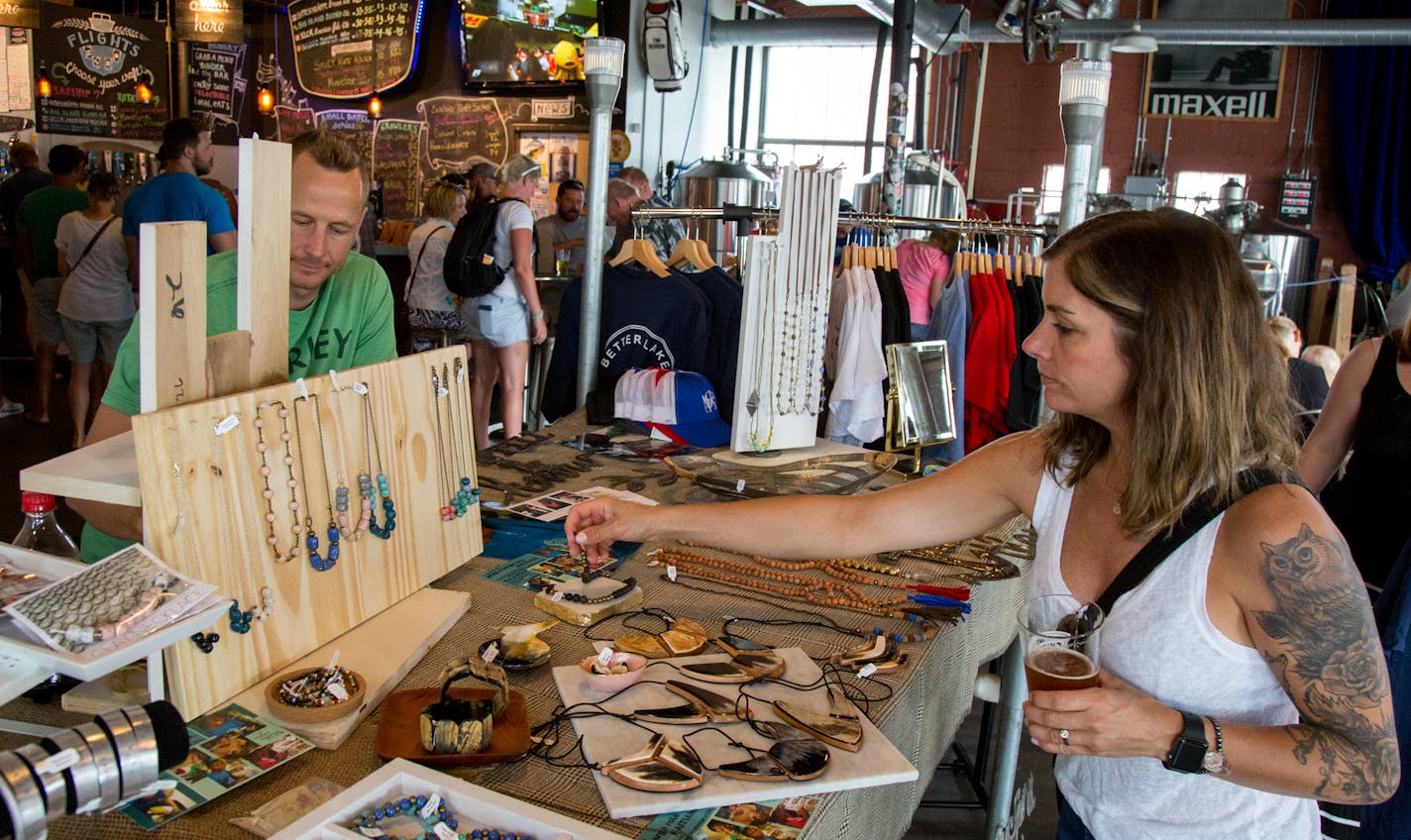 Mari Anderson looks at jewelry handmade in Haiti sold by Jesse Farley (left) from Gathered Goods Co. during the Crafts & Drafts Summer Craft Fair.