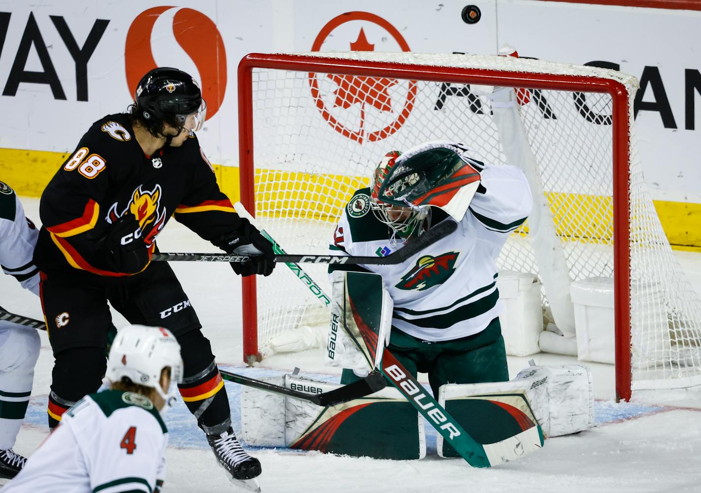 Minnesota Wild goalie Filip Gustavsson, right, deflects the puck over the net as Calgary Flames forward Andrew Mangiapane watches during the second period of an NHL hockey game Saturday, March 4, 2023, in Calgary, Alberta. (Jeff McIntosh/The Canadian Press via AP)