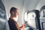 Connection in the airplane. Young man (traveler) using smart phone during flight and listening music.