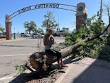 woman sitting on downed tree with "Downtown Bemidji" arch in background