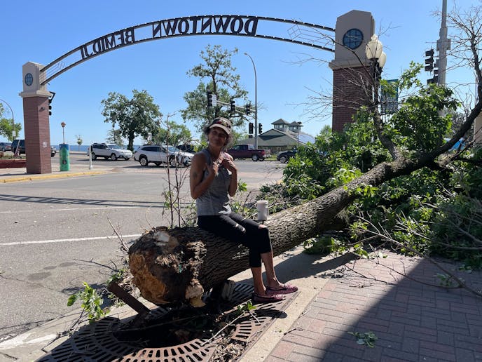 woman sitting on downed tree with "Downtown Bemidji" arch in background