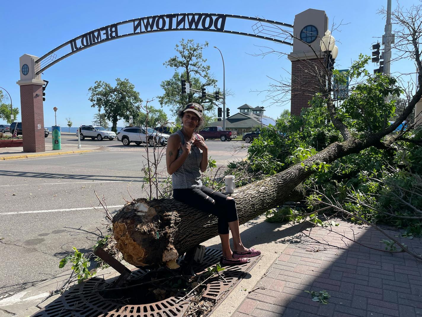 woman sitting on downed tree with "Downtown Bemidji" arch in background