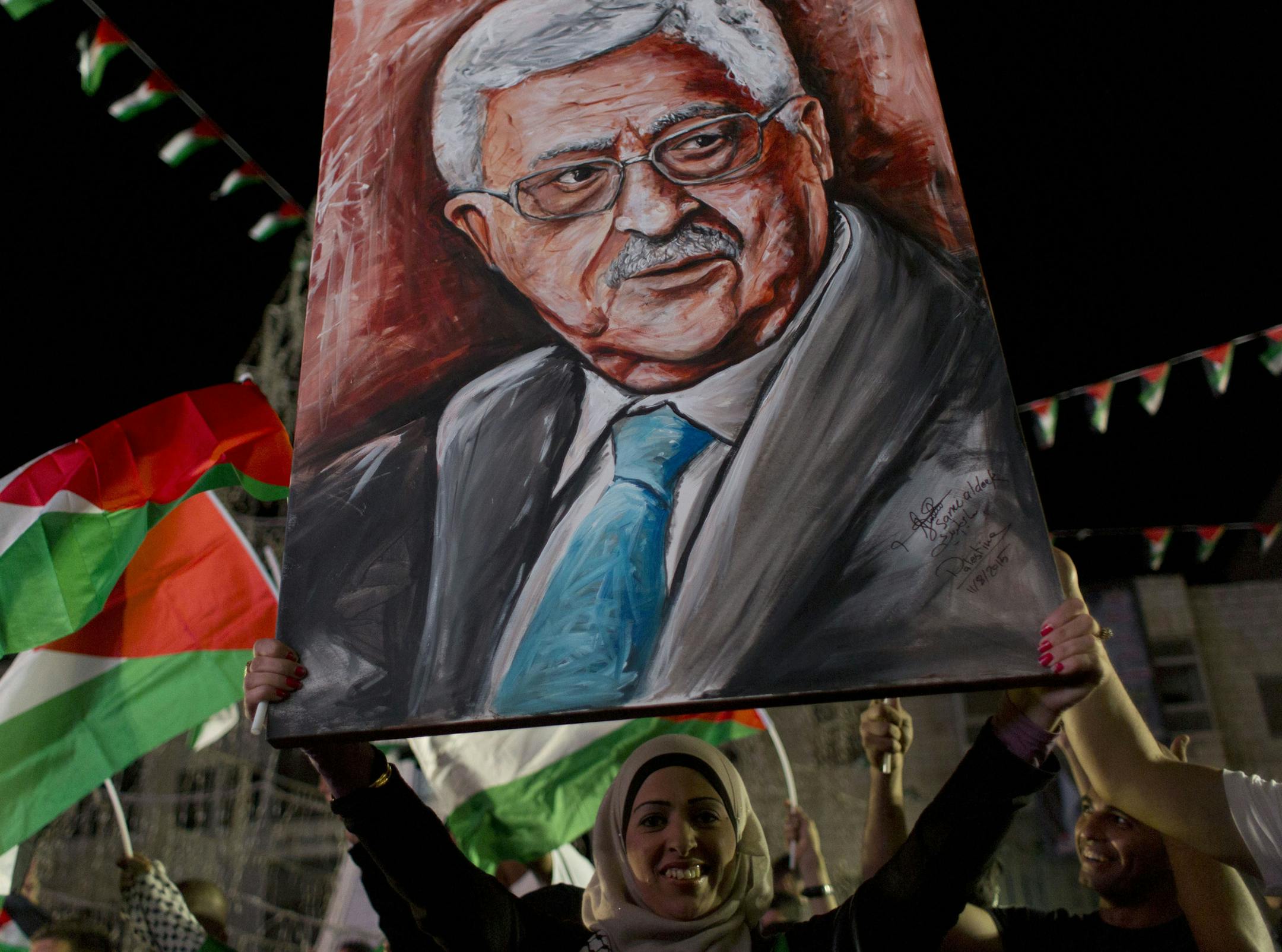 A woman carries a painting of Palestinian President Mahmoud Abbas as others fly their national flags following his speech at the U.N. General Assembly shown on TV in the West Bank city of Ramallah, Wednesday, Sept. 30, 2015. Palestinian President Mahmoud Abbas declared before world leaders Wednesday that he is no longer bound by agreements signed with Israel, and called on the United Nations to provide international protection for the Palestinian people. (AP Photo/Nasser Nasser)