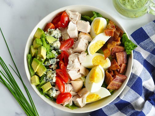 A big bowl of Cobb salad — lettuce topped with avocado, cheese, chicken, eggs and bacon with avocado green goddess dressing.