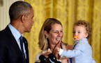President Barack Obama, left, gets a high five from Oliver Reeve, right, the son of Minnesota Lynx coach Cheryl Reeve, center, in the East Room of the