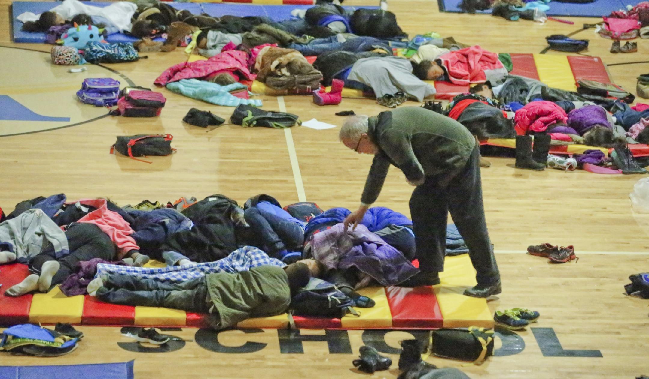 A teacher at E. Rivers Elementary School covers sleeping children in the school's gym in Atlanta, Jan. 29, 2014. A storm deposited less than three inches of snow throughout the Atlanta region on Tuesday, but it left roads impassable, drivers trapped in cars overnight and children stuck in schools Wednesday morning. (John Spink/Atlanta Journal Constitution) -- NO SALES