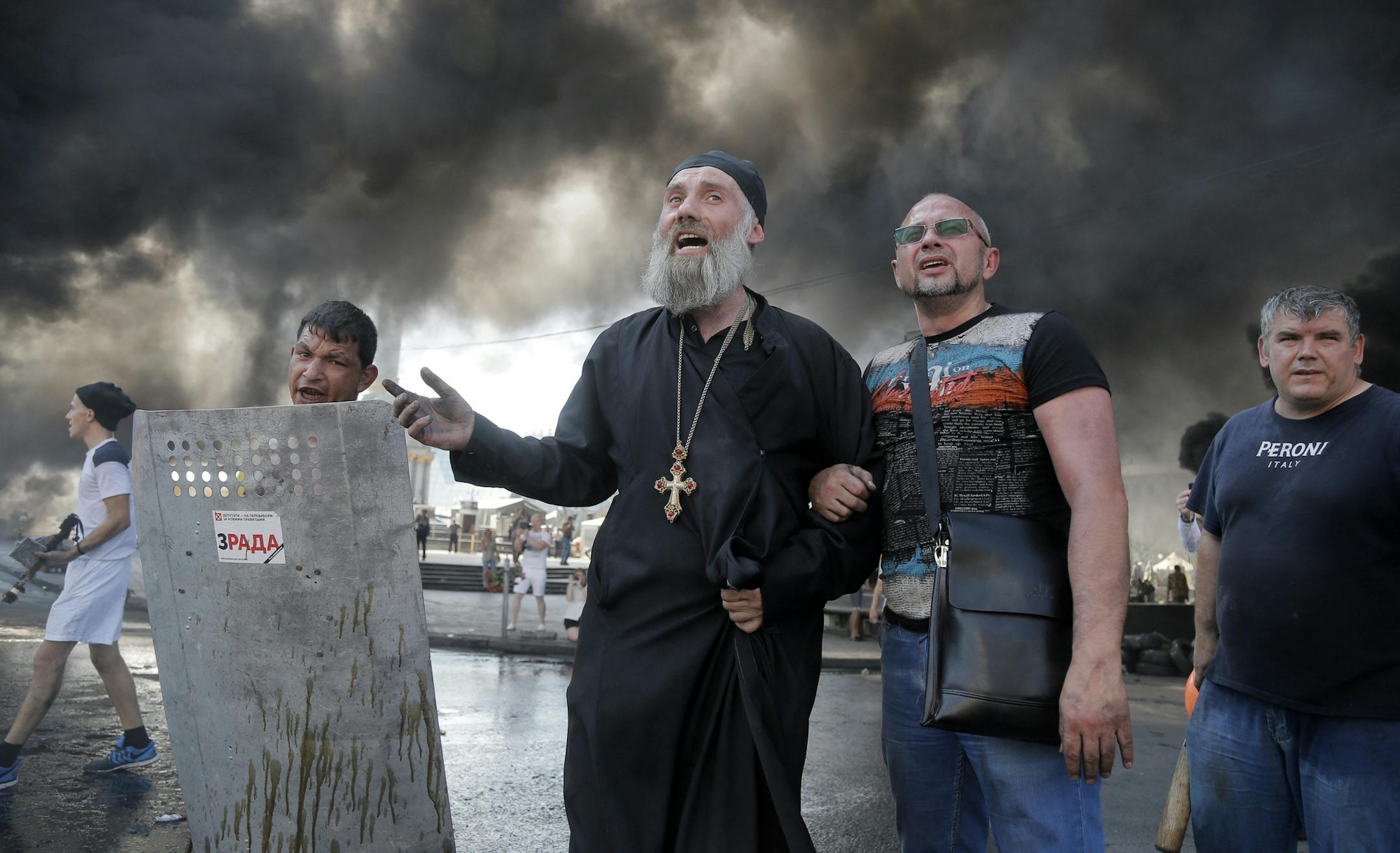 Activists shout during clashes with forces from the Kiev-1 volunteer battalion on Independence Square in Kiev, Ukraine, Thursday, Aug. 7, 2014. Demonstrators on Thursday confronted city workers attempting to clear a central square, lighting tyres on fire in protest against the city government's move. Dark plumes of smoke from burning rubber rose above Independence Square as workers guarded by armed men in camouflage dismantled some of the barricades surrounding the area. (AP Photo/Efrem Lukatsky