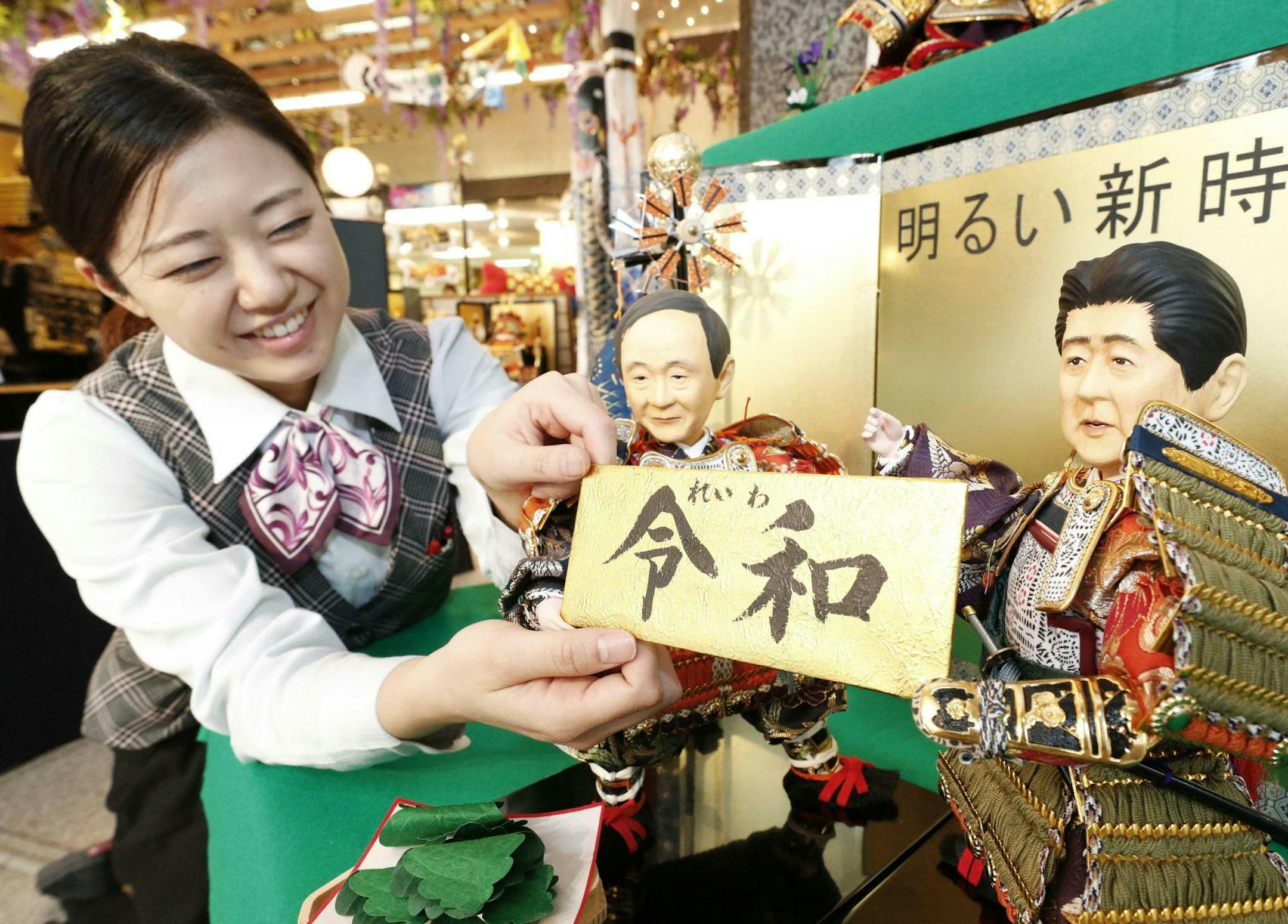 A shop worker arranges Japanese traditional dolls depicting Japanese Chief Cabinet Secretary Yoshihide Suga, left, and Japanese Prime Minister Shinzo Abe, right, holding the new era name "Reiwa" at Kyugetsu, a Japanese doll company, in Tokyo, Monday, April 1, 2019. Japan's government has unveiled an era name, "Reiwa," or "pursuing harmony," for soon-to-be Emperor Naruhito, who will succeed the Chrysanthemum throne on May 1. His father, Emperor Akihito, is abdicating, with his "Heisei" era coming