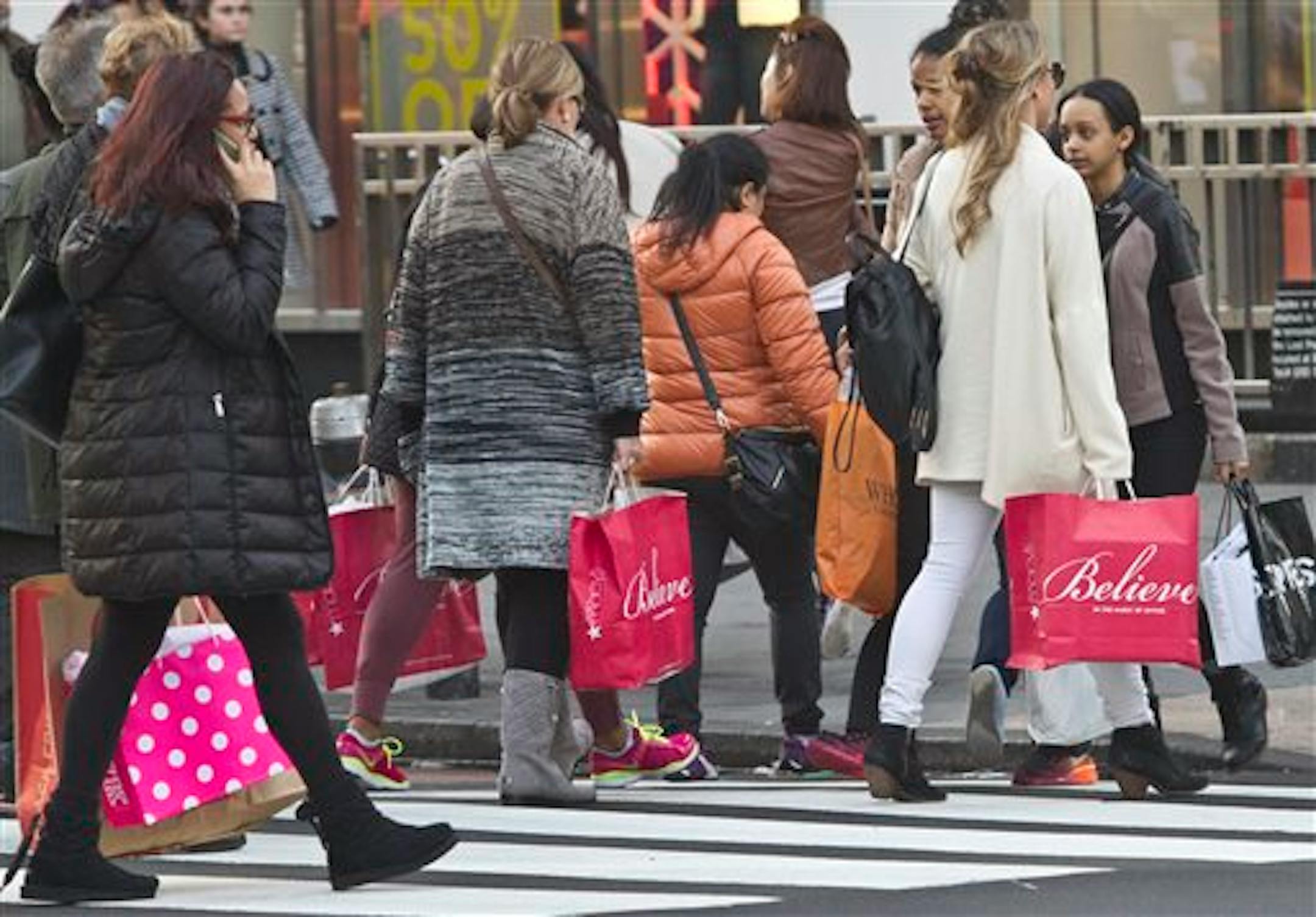 Shoppers carry bags as they cross a pedestrian walkway near Macy's in Herald Square, Friday, Nov. 27, 2015, in New York. The early numbers aren't available yet on how many shoppers headed out to stores on Thanksgiving, instead of waiting until today. But it's expected that more than three times the number who shopped yesterday will be out bargain-hunting today.(AP Photo/Bebeto Matthews)
