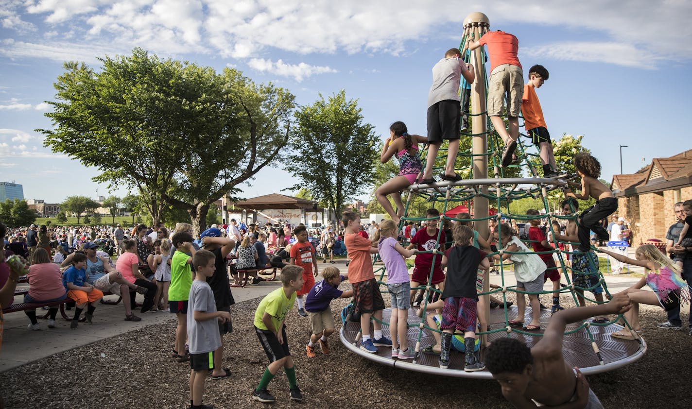 Children played on the playground equipment next to the large crowd watching the Johnny Holm Band perform on stage at the Summertime by George outdoor concert on June 13 in St. Cloud.