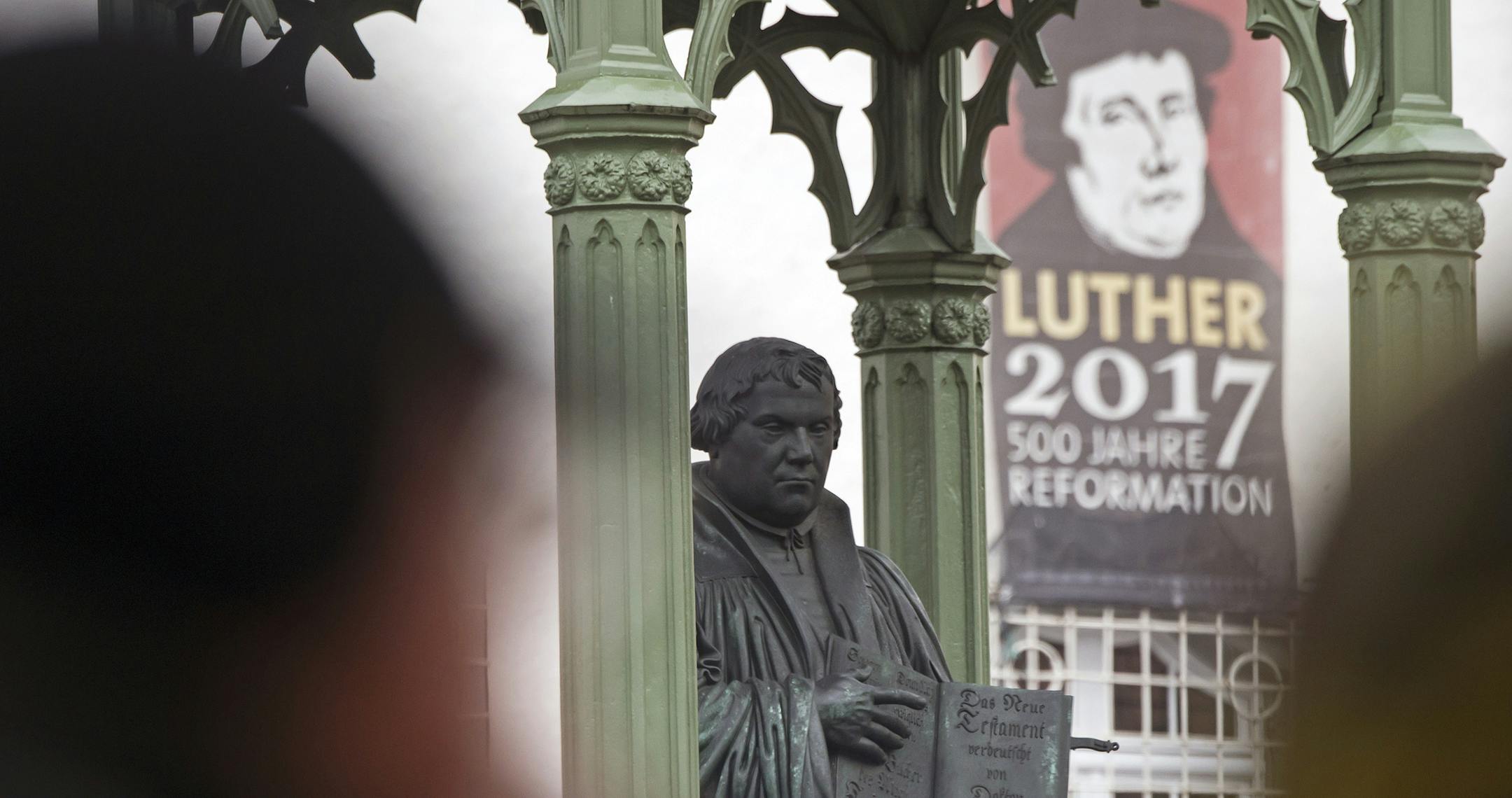 Visitors walk in front of the Martin Luther monument prior the celebrations on the occasion the 500th Anniversary of the Reformation in Wittenberg, Germany, Tuesday, Oct. 31, 2017. German will leaders mark the 500th anniversary of the day Martin Luther is said to have nailed his theses challenging the Catholic Church's practice of selling indulgences to a church door, a starting point of the Reformation. (AP Photo/Jens Meyer)