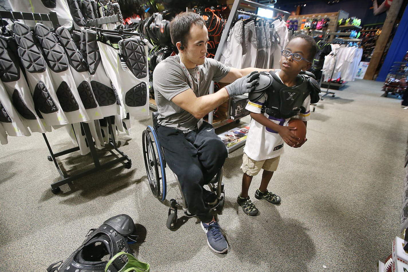 Chuck Aoki, a paralympic rugby player, helped Givenson Thimjon, 6, cq, with shoulder pads during his shift at Dick's Sporting Goods, Friday, July 15, 2016 in Richfield, MN. Dick's Sporting Goods has a program in which it hires Olympic and Paralympic hopefuls and allows them to schedule hours around their training and competition schedules. ] (ELIZABETH FLORES/STAR TRIBUNE) ELIZABETH FLORES &#x2022; eflores@startribune.com ORG XMIT: MIN1607151110551422