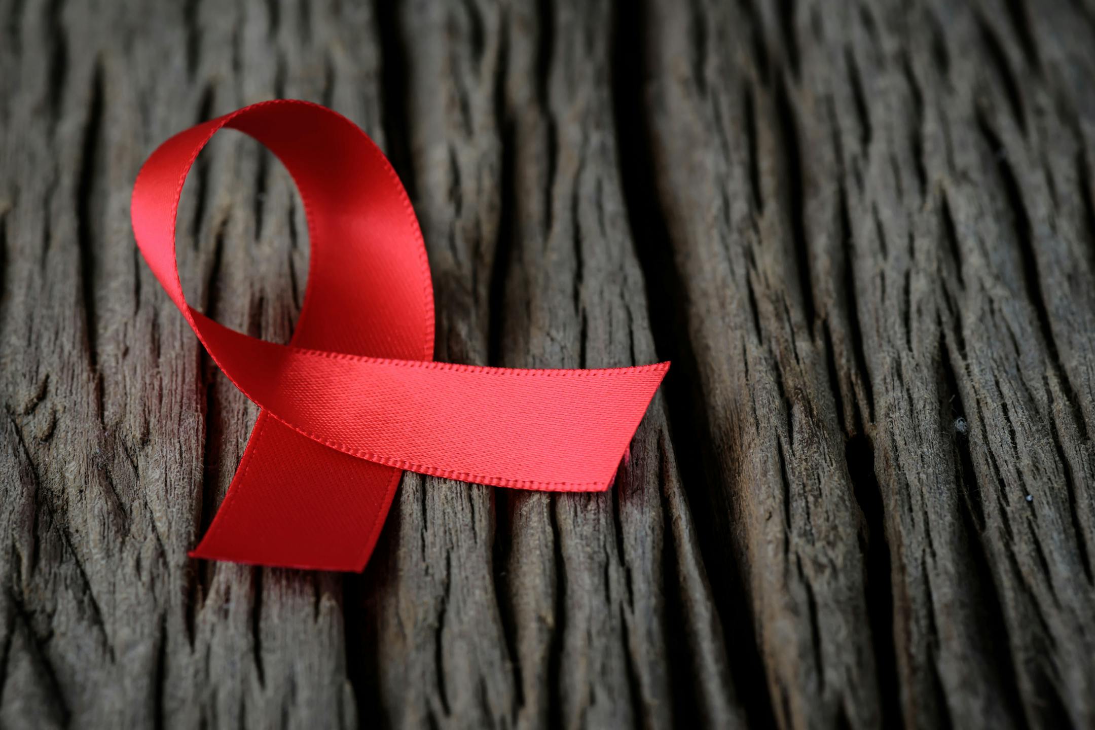 Red ribbon on wooden background for World Aids day awareness campaign.