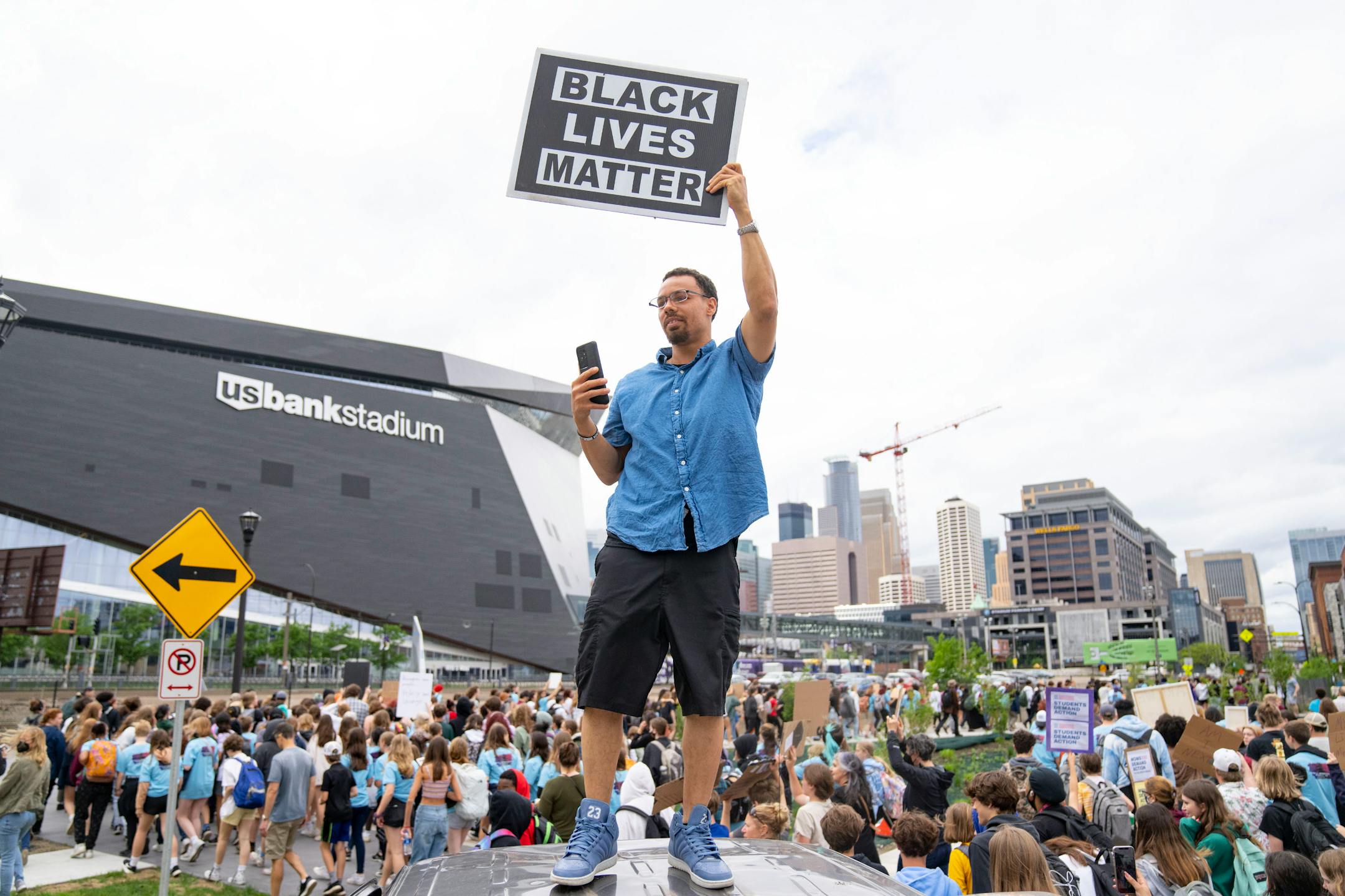 Todd Gramenz holds up a sign and records a video as hundreds of students from around the Twin Cities march to U.S. Bank Stadium.