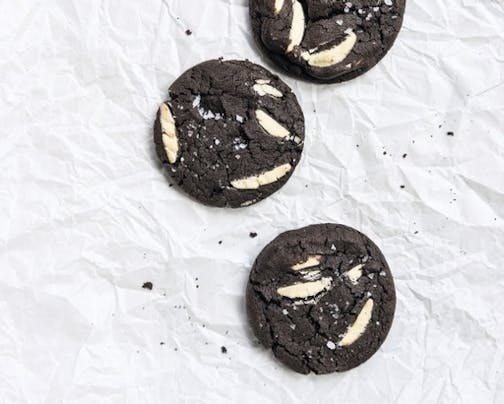 Three dark chocolate cookies with white chocolate chips are spread out on a quarter sheet pan.