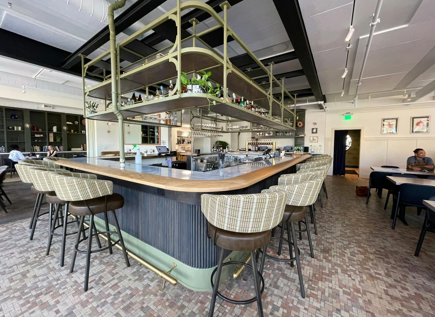 The corner bar of Lynette with open, gold tiered shelves and round, plaid bar stools.