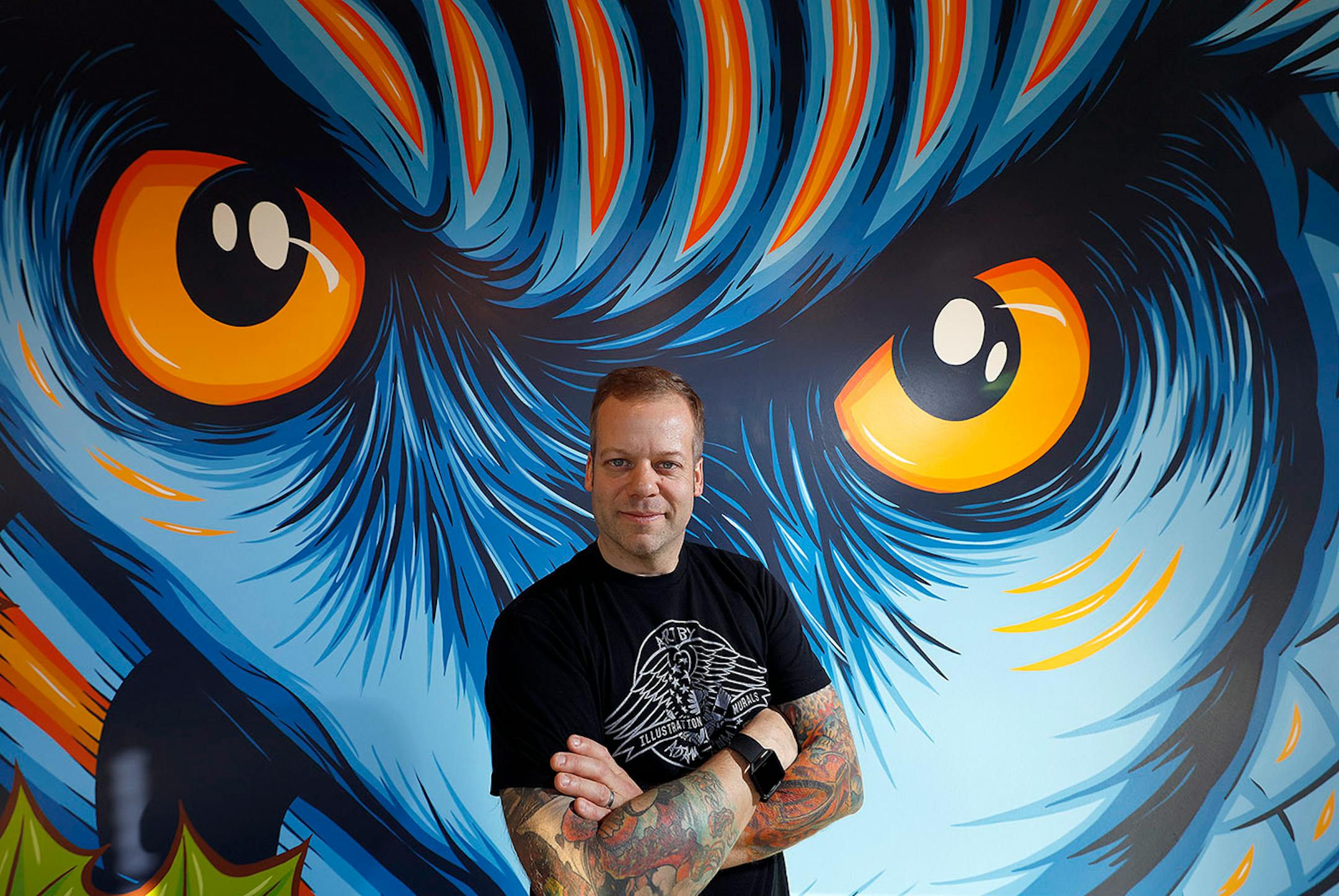 The everywhere artist, Adam Turman, His clean, dynamic murals crawl up the sides of breweries, in elementary schools, the lobby of downtown Minneapolis' hip, new hotel. He boasts T-shirts and pint glasses and posters. He's even created a jigsaw puzzle. Here, Adam Turman in front of his owl mural. The mural is located at the A-Mill Artist Lofts, Minneapolis.