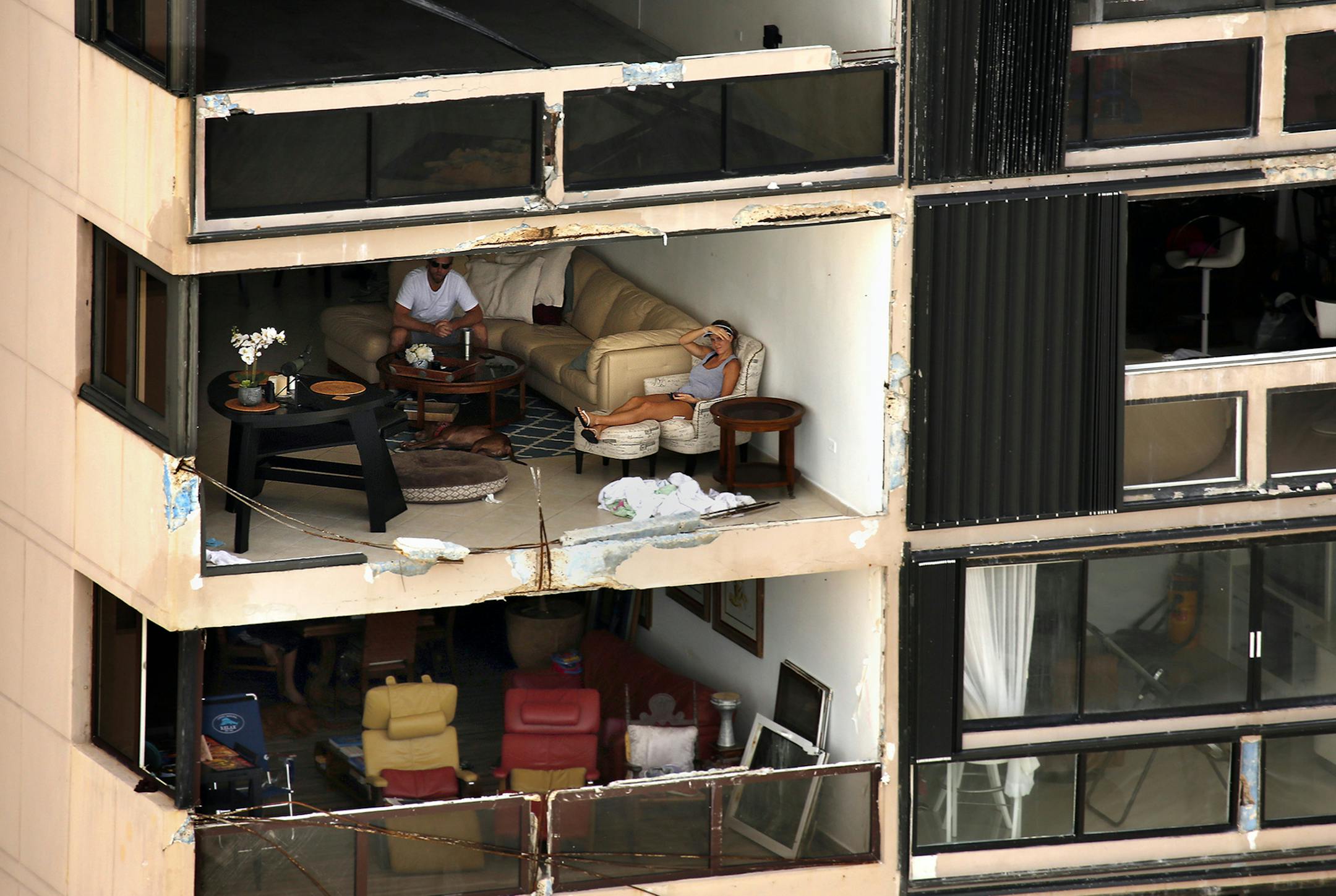 Two people sit in an apartment with a wall missing along the waterfront on Sept. 25, 2017 in San Juan. Nearly one week after hurricane Maria devastated the island of Puerto Rico, residents are still trying to get the basics of food, water, gas, and money from banks. Much of the damage done was to electrical wires, fallen trees, and flattened vegetation, in addition to home wooden roofs torn off. (Carolyn Cole/Los Angeles Times/TNS)
