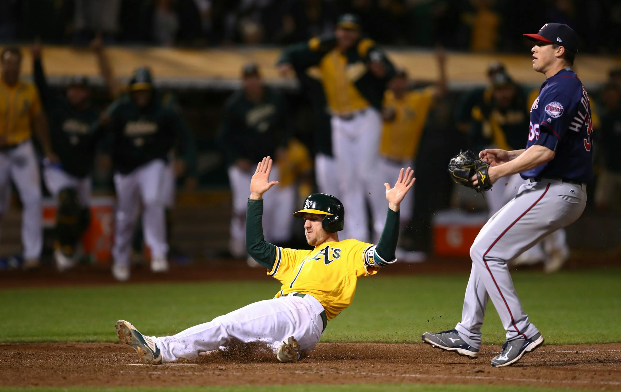 After a bases-loaded wild pitch, Stephen Piscotty slides to score in front of the Twins' Trevor Hildenberger in the ninth inning