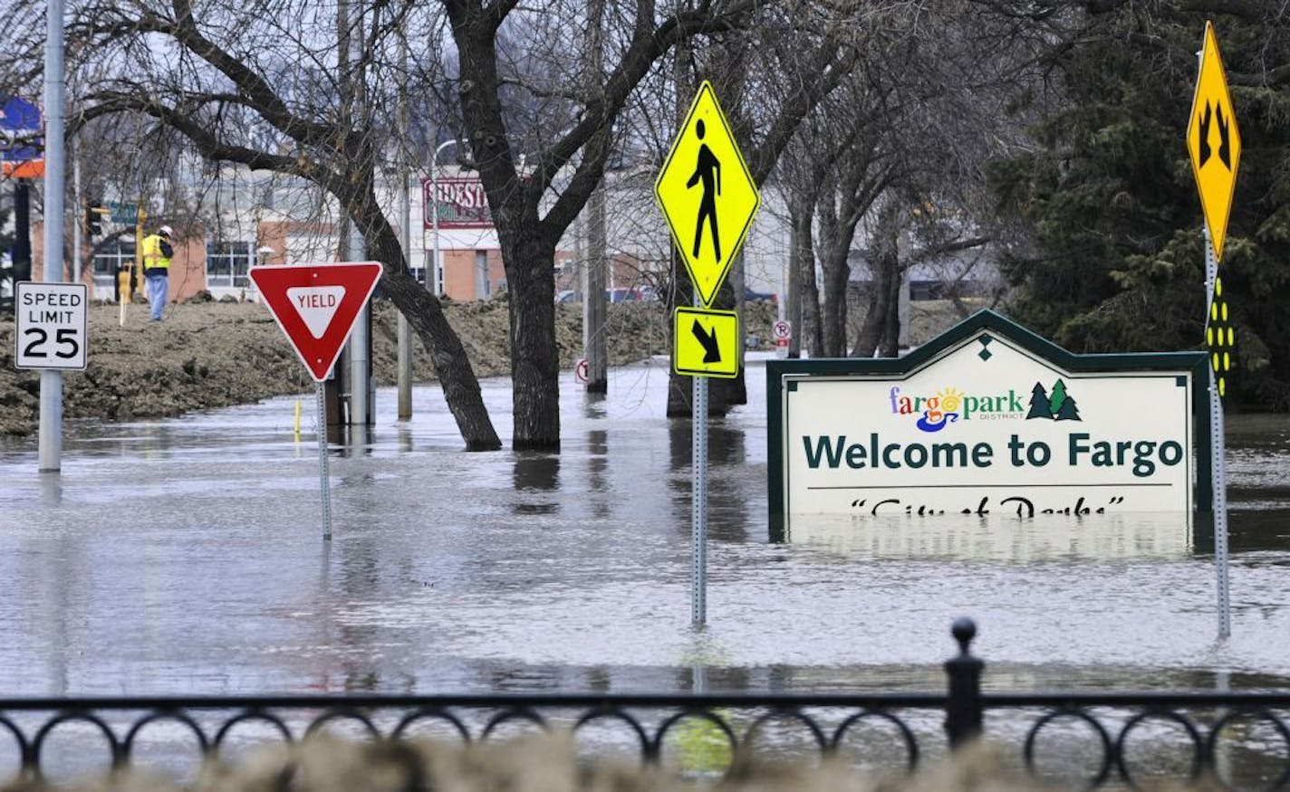 FILE - In this April 8, 2011 file photo, a welcome sign for Fargo, N.D., sits in the rising floodwaters of the Red River as a flood engineer for the U.S. Army Corps of Engineers, at left, inspects the levee protecting the downtown area. The decision by the Buffalo Red River Watershed District in Minnesota to back out of an agreement for a Red River diversion project around the Fargo area has raised questions about permits for the $2.1 billion channel. (AP Photo/Jim Mone, File) ORG XMIT: MIN20160