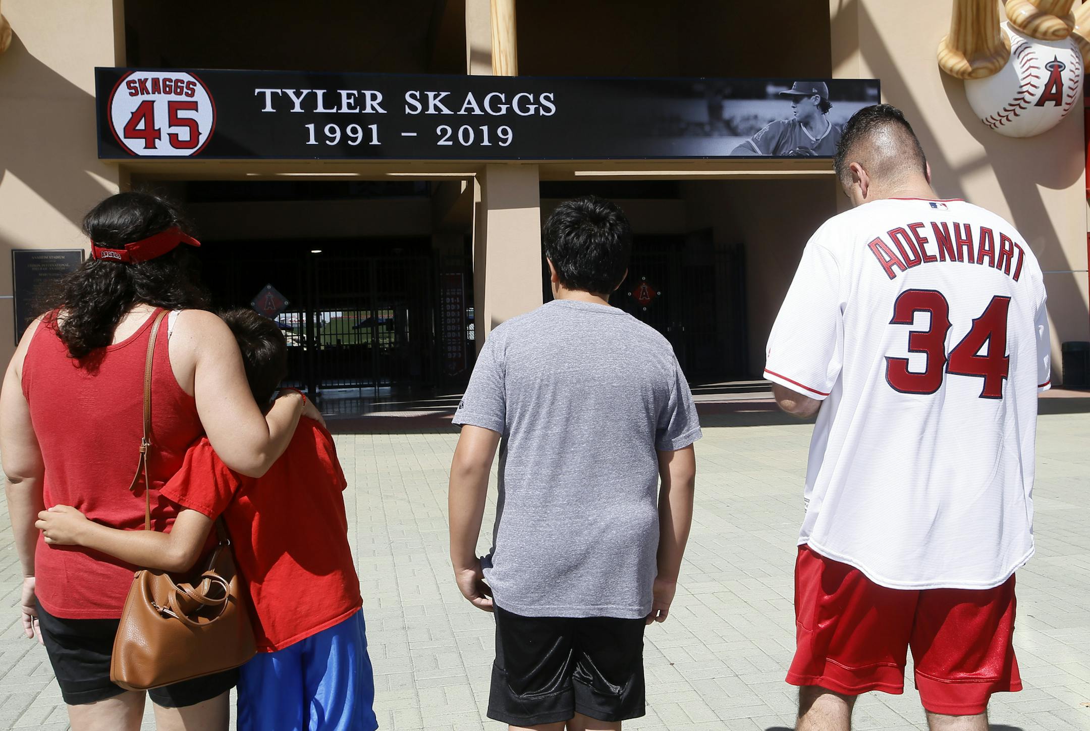 Ben Villa, his wife, Cindy, left, with their sons' Alex, second from left, and Benji give their condolences for pitcher Tyler Skaggs at Angel Stadium in Anaheim, Calif., Monday, July 1, 2019. Skaggs died at the age of 27, stunning Major League Baseball and leading to the postponement of the team's game against the Texas Rangers on Monday. Villa wears a jersey for the last Angel to die Nick Adenhart, who died during the baseball season in 2009. (AP Photo/Alex Gallardo)