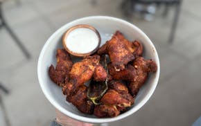 A white bowl of dry rub wings. The wings have a tanned, orangey hue with black specks of pepper and a char roasted jalepeno in the middle. On the side