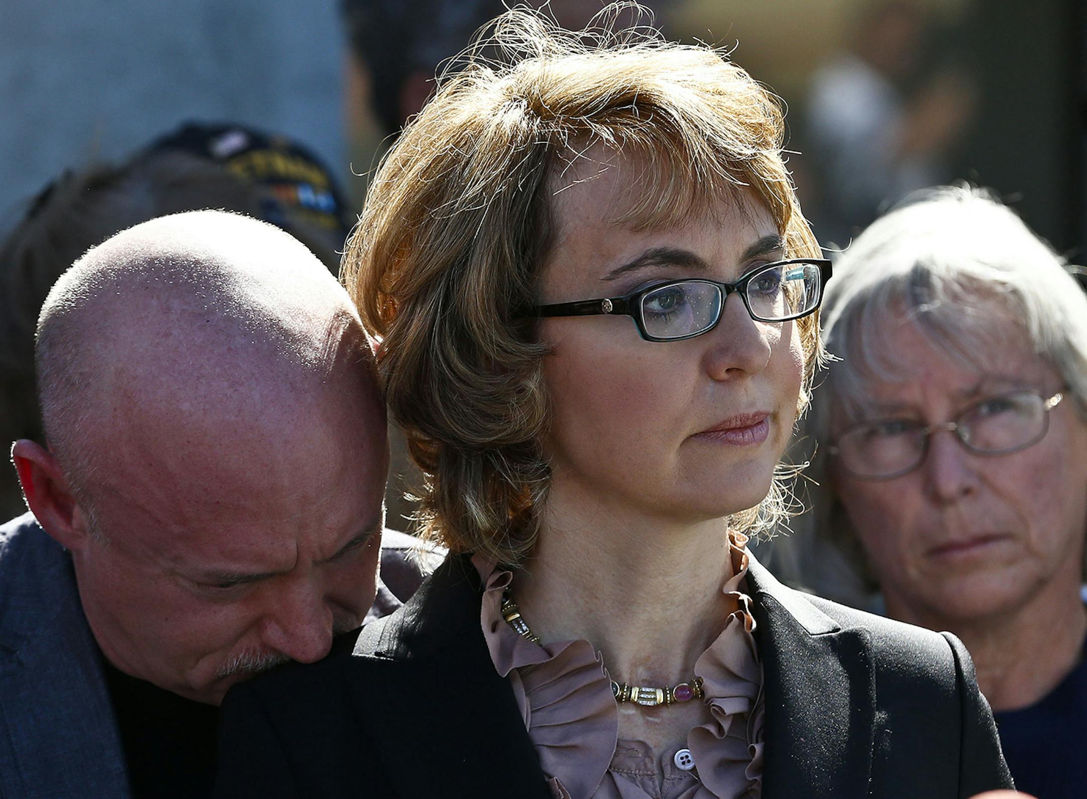 Former Rep. Gabrielle Giffords, center, is joined by her husband Mark Kelly, left, and Emily Nottingham, mother of shooting victim Gabe Zimmerman, listening to a speaker as they returned to the site of a shooting that left her critically wounded to urge key senators to support expanded background checks for gun purchases, Wednesday, March 6, 2013, in Tucson, Ariz. (AP Photo/Ross D. Franklin) ORG XMIT: MIN2013041811364892 ORG XMIT: MIN1304181143121634