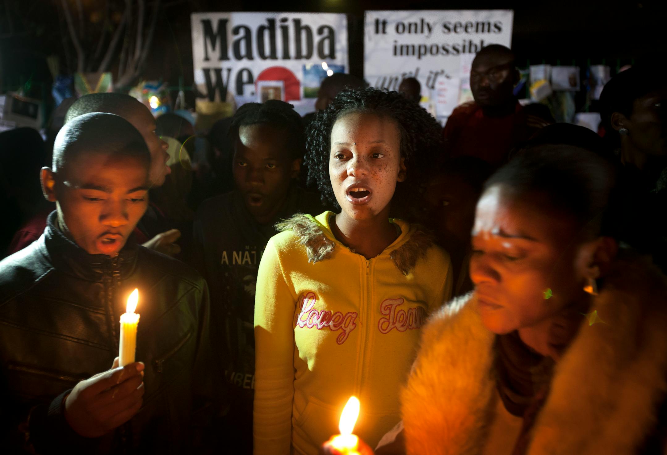 Well wishers sing songs by candlelight to show their support at night outside the entrance to the Mediclinic Heart Hospital where former South African President Nelson Mandela is being treated in Pretoria, South Africa Thursday, June 27, 2013. Nelson Mandela's health improved overnight and his condition remains critical but is now stable, the South African government said Thursday in a statement that brought a measure of relief to the country. (AP Photo/Ben Curtis)