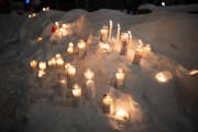 Lit candles in glass containers in snowbank.