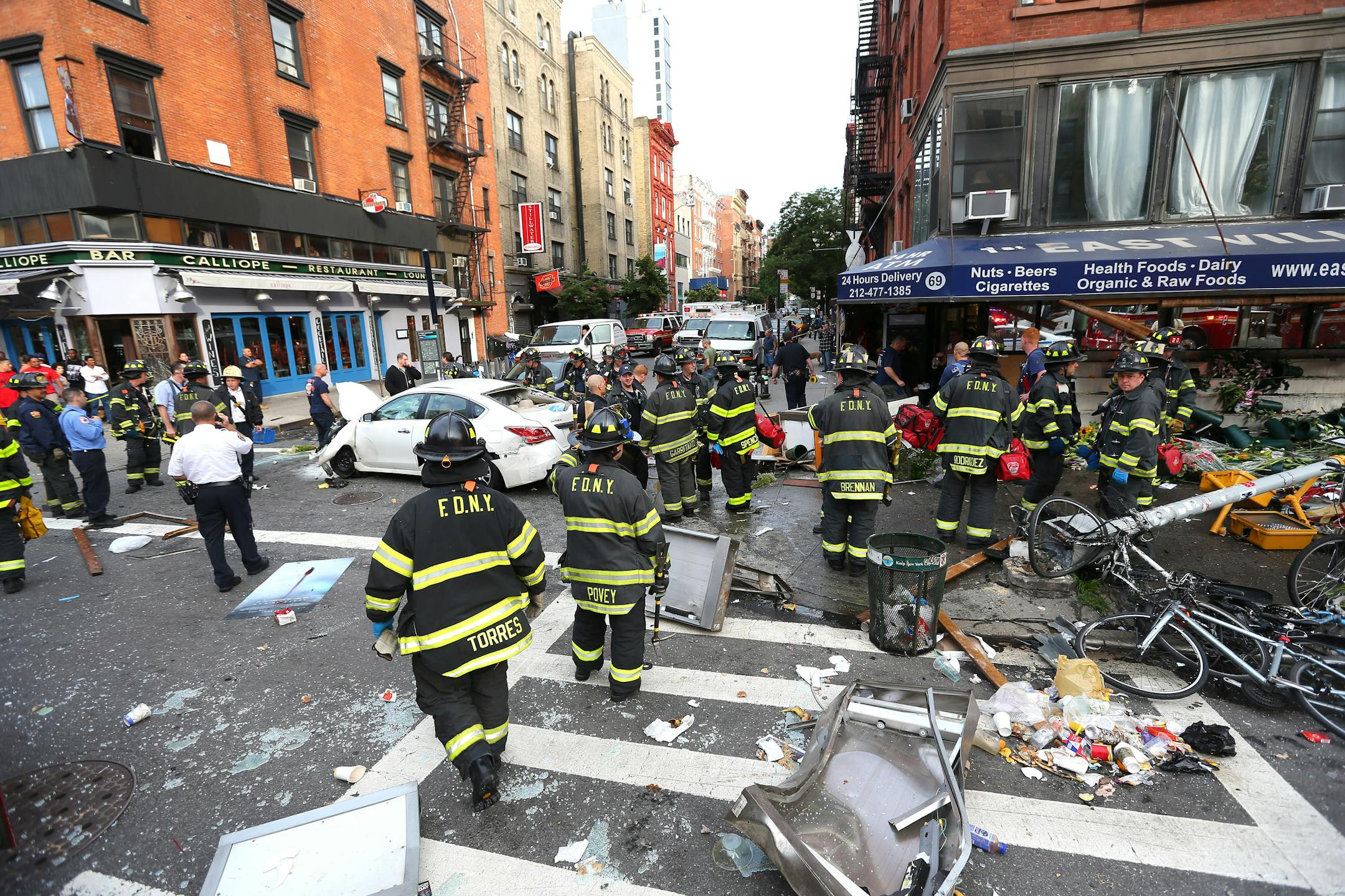 A white Nissan Altima, center, that jumped a curb in Lower Manhattan in front of the grocery with the blue awning, in New York, June 19, 2013. At least eight people were injured Wednesday morning after the car jumped the curb in front of a corner bodega, leaving behind a trail of mangled bicycles, broken glass and other debris.