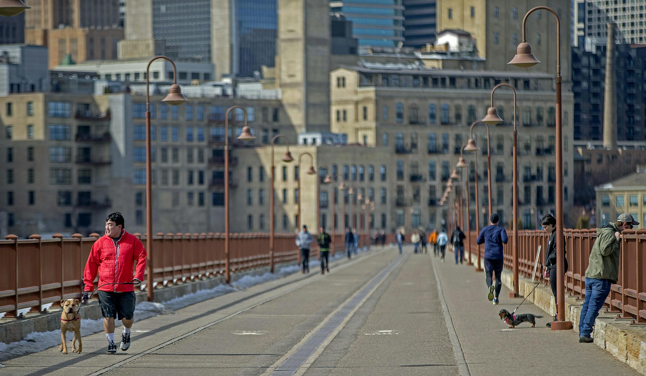 Warmer temperatures brought many out during the lunch hour, including Patrick Groschan, braving shorts, left, and his dog "Rex," as they made their way across the Stone Arch Bridge, Friday, March 16, 2018 in Minneapolis, MN. ] ELIZABETH FLORES ï liz.flores@startribune.com