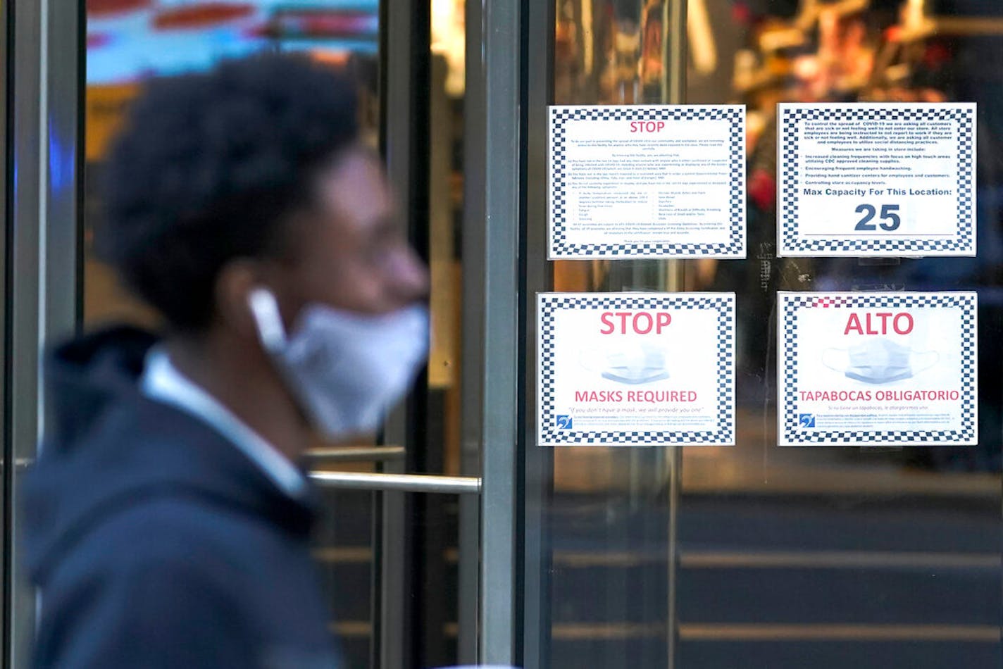 A pedestrian walked past bilingual COVID-19 precaution signs outside a retail store on Michigan Avenue in Chicago on Nov 18.