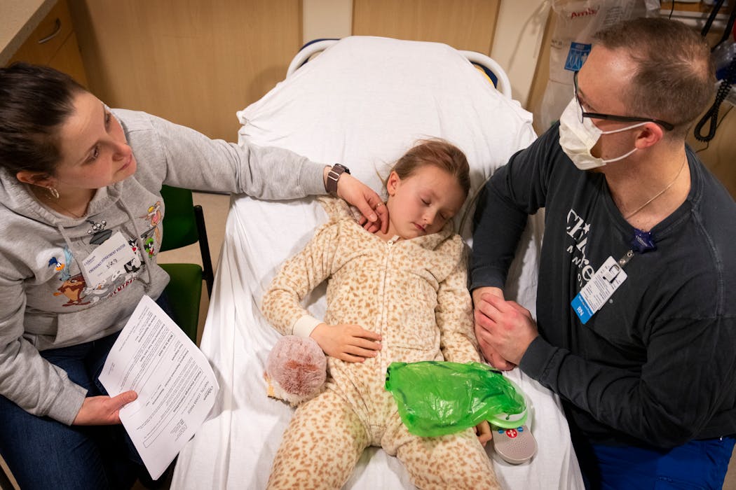 Registered nurse Joe Schwartz, right, talks over the discharge paperwork with Amanda Martin, left, mother of patient Leiana Martin, 5, center, who was diagnosed with strep and flu, on March 27.