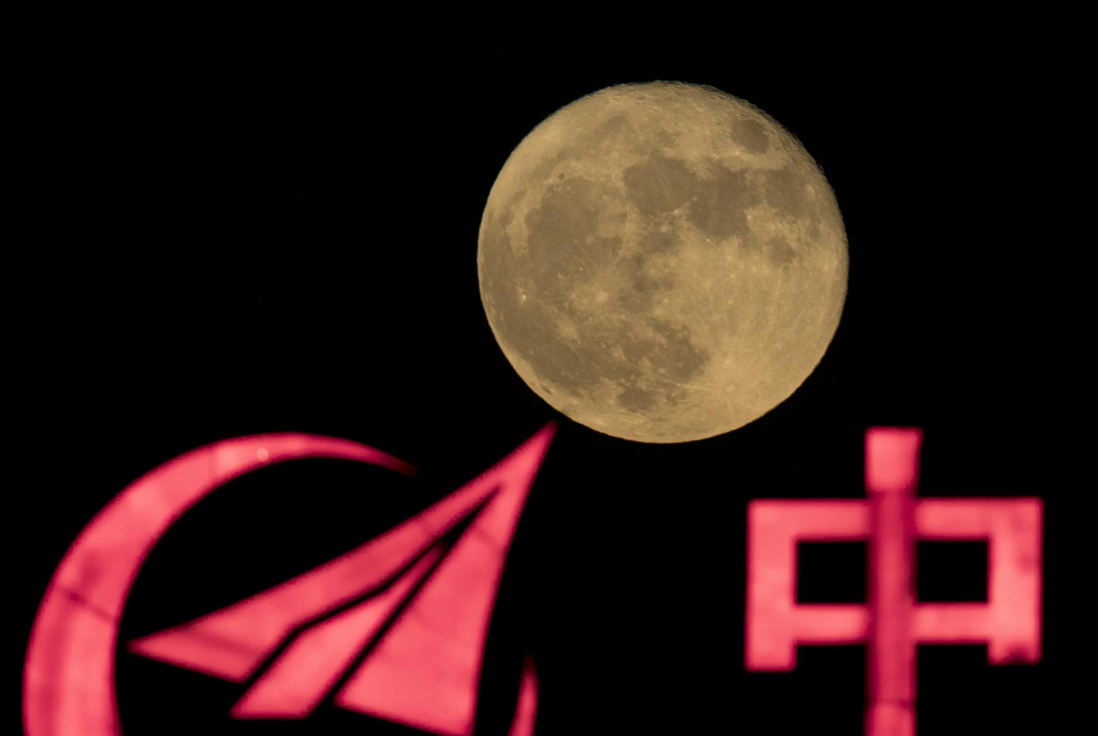 The supermoon rose Tuesday over a logo for a Chinese state-owned enterprise with part of the word for "China" in Beijing.