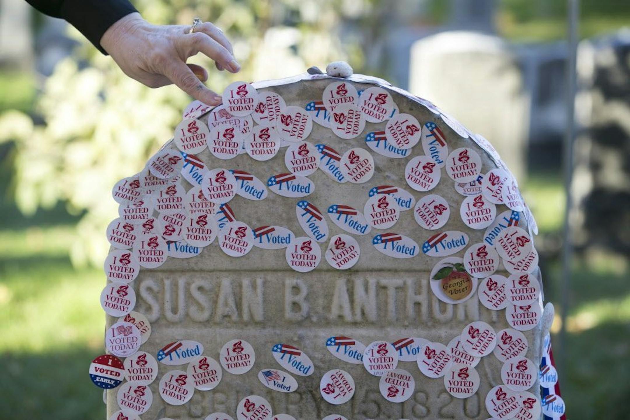 A woman places a voting sticker on the headstone of Susan B. Anthony, a women's suffrage pioneer, on Election Day in Rochester, N.Y., Nov. 8, 2016.