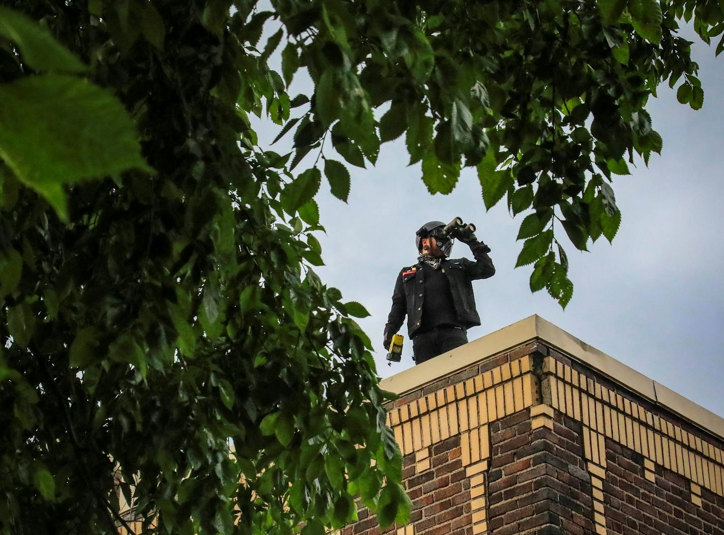 Obediah, a member of a neighborhood watch that started after the death of George Floyd in police custody sparked unrest, looks out from the roof of his home with binoculars, Tuesday June 2, 2020, in Minneapolis, Minn. A week of civil unrest has led some Minneapolis residents near the epicenter of the violence to take steps to protect their homes and neighborhoods. (AP Photo/Bebeto Matthews) ORG XMIT: MER60037765649c1890de1ae19fb8b3d