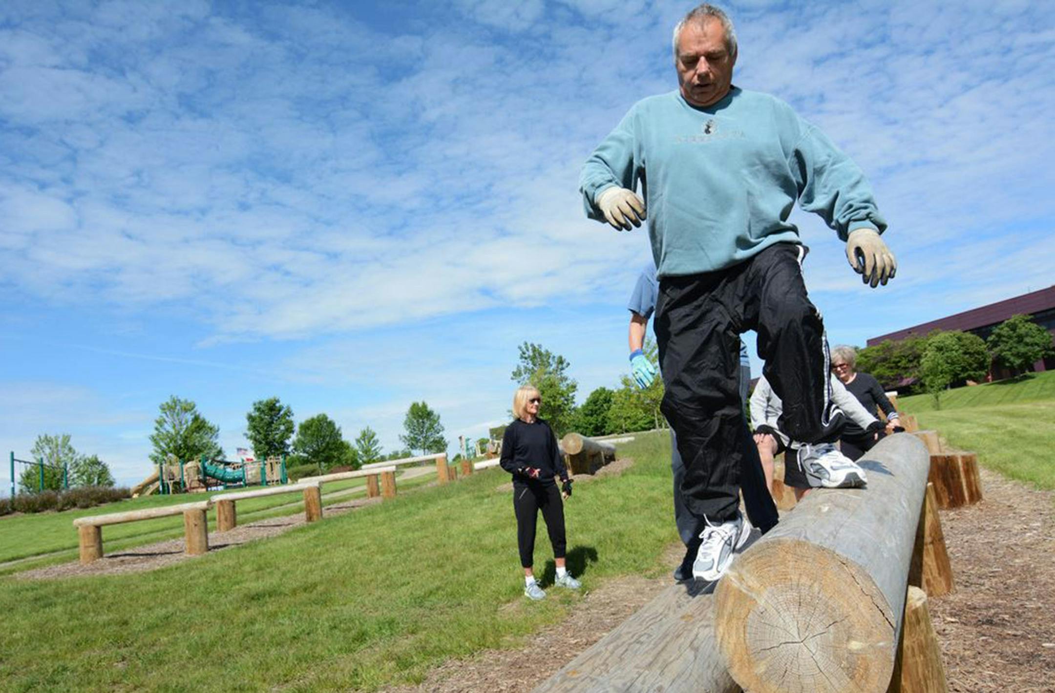 Tom Blunt, of Eagan, climbed on a log formation at the fitness area at Eagan Central Park. Instructor Jill Greenan is pictured in the background.