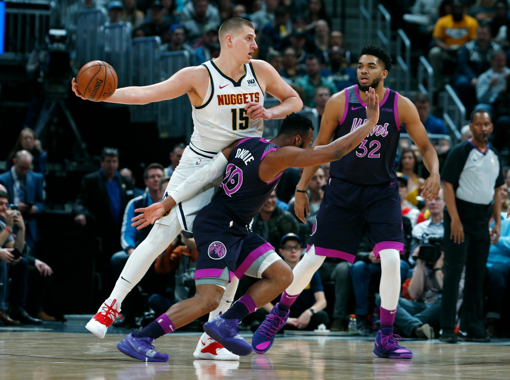 Denver Nuggets center Nikola Jokic, back left, looks to pass the ball as Timberwolves guard Josh Okogie, left front, and center Karl-Anthony Towns defend in the first half