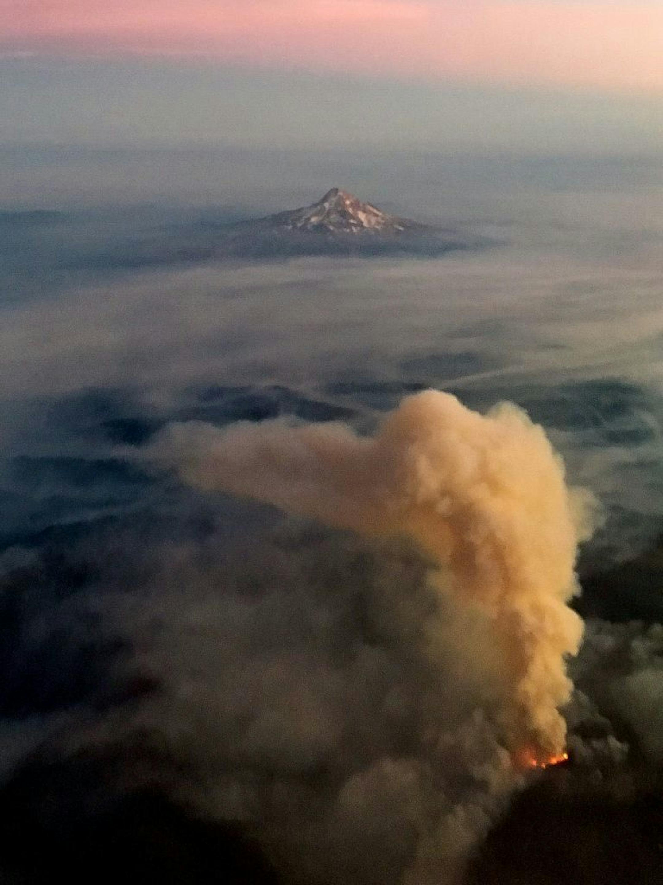 Mt. Hood is visible beyond a raging wildfire in as seen from a flight between Minneapolis and Oregon on Monday, Sept. 12, 2017.