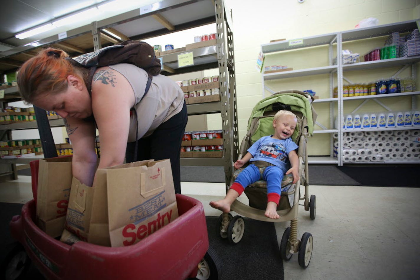 Tara Nordgren (with her son Allan) filled grocery bags at the Anoka County Brotherhood Council food shelf in Anoka, Minn., on Thursday, June 18, 2015. Nordgren, who works at Burger King, needs help with groceries since her food stamps were cut back.