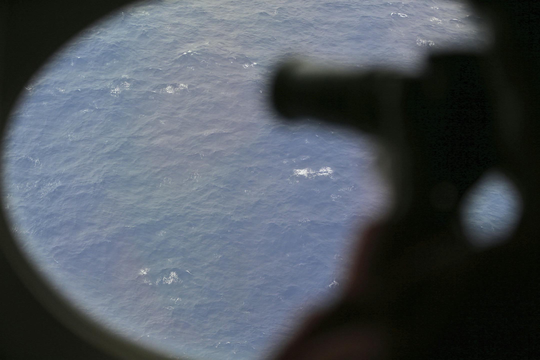 An observer on a Japan Coast Guard Gulfstream aircraft takes photos out of a window while searching for the missing Malaysia Airlines Flight MH370 in Southern Indian Ocean, near Australia, Tuesday, April 1, 2014. Bad weather and poor visibility caused the search to be called off early with the coast guard plane only completing one of its three 210 nautical mile legs. (AP Photo/Rob Griffith, Pool)